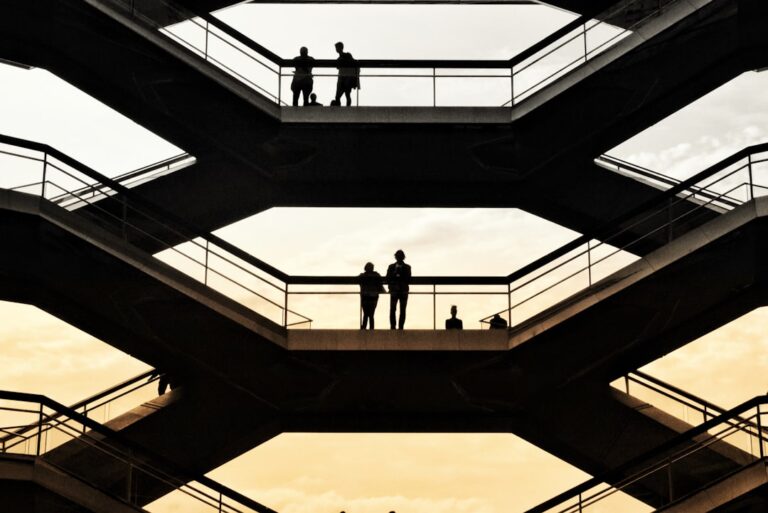 Silhouetted people stand on geometric platforms against a sunset sky, echoing NYC's architectural beauty and attention to detail, akin to Gramercy Cleaners' precision.